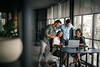 Group of young professionals gathered around laptop in modern office